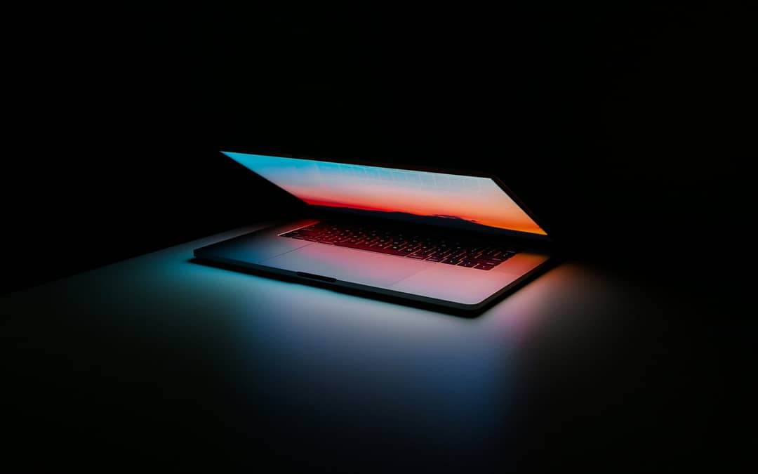 Poluotvoreni laptop s zaslonom koji prikazuje šarene svjetlosne odsjaje, smješten na tamnoj podlozi.